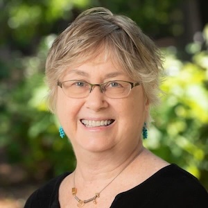 Smiling woman with glasses and turquoise earrings.