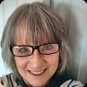 Smiling woman with glasses and gray hair.