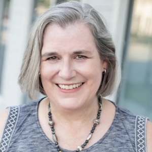 Smiling woman with gray hair wearing necklace.